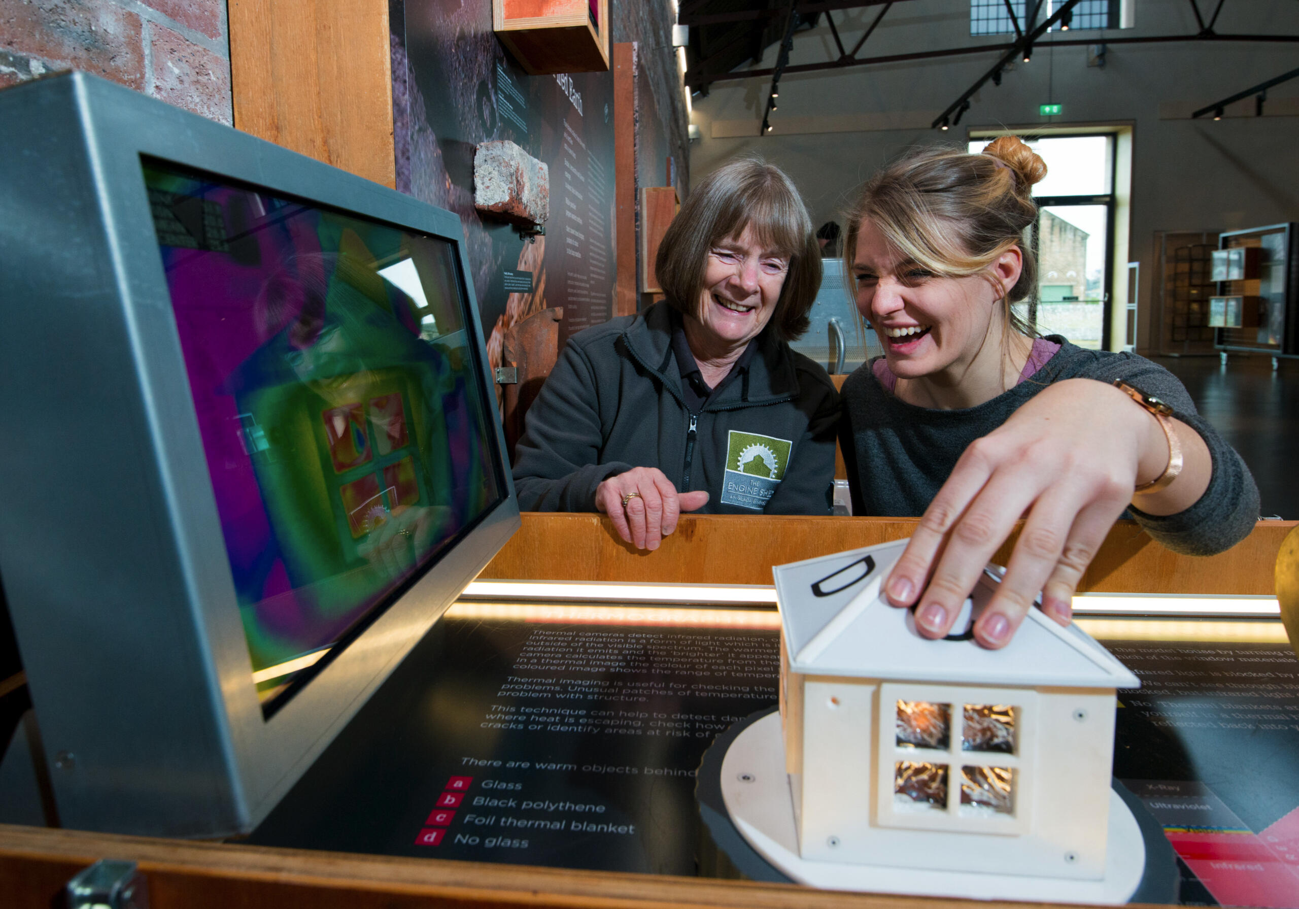 Photo, from Historic Environment Scotland, of a volunteer and a visitor interacting with a museum display joyfully.